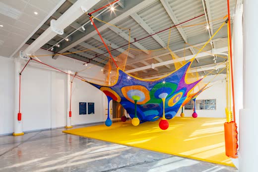 OliOli: a crocheted rainbow net suspended over a yellow play floor